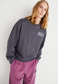 Felpa grigia con scollatura rotonda, caratterizzata da un logo "Star Wars". Abbinata a pantaloni della tuta viola chiaro, raccolti in vita.
