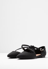 Zwarte ballet flats met een spitse neus, gemaakt van een gladde stof, voorzien van gekruiste banden en een kleine enkelgesp. Minimalistisch ontwerp zonder patronen.
