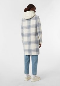 Cappotto in misto lana con motivo a griglia grigio chiaro e bianco, dotato di cappuccio imbottito color crema, abbinato a jeans azzurri e sneakers bianche.