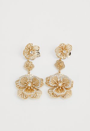 Boucles d'oreilles en tone or avec des motifs floraux présentant des découpes intriquées agrémentées de cristaux, mettant en valeur des pétales en trois dimensions et un délicat travail de détails.