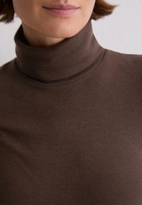 Brauner gerippter Rollkragenpullover mit figurbetonter Passform, aus weichem Material, mit einem hohen Kragen und glatter Textur.