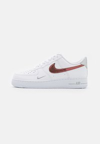 Vita Nike Air Force 1-sneakers med en slät läderövre del, med en metallisk kopparswoosh, silverdetaljer och en texturerad gummisula.