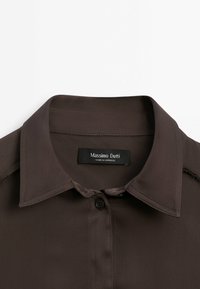 Chemise marron foncé à col avec des boutons noirs et une étiquette mentionnant Massimo Dutti fabriqué au Maroc.