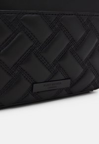 Borsa a tracolla in pelle tessuta nera con motivo trapuntato, dotata di un'etichetta metallica discreta che riporta "Kurt Geiger London" in hardware nero lucido.