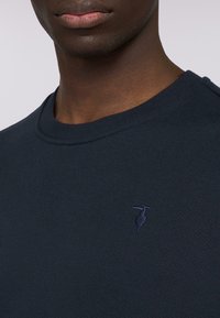 T-shirt a coste di colore navy realizzato in un tessuto misto cotone, con un piccolo logo di un airone ricamato sul petto e scollatura a girocollo.