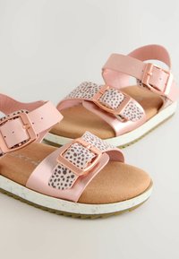 Sandali in eco-pelle rosa con due cinghie regolabili, dettagli in tessuto a pois, suola imbottita e fibbie in oro rosa.