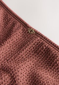 Gros plan sur un tissu mauve texturé avec des motifs en zigzag complexes et une petite boucle métallique ronde attachée près d'un bord froncé.