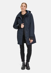 Navy wasserfester Parka mit Kapuze, Knopf- und Reißverschlussverschluss, zwei Seitentaschen und einem leichten, gesteppten Material.