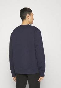 Navy blue sweatshirt, crew neck, long sleeves, ribbed cuffs and hem, smooth texture, plain design, worn with black pants.