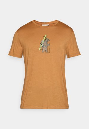 Kurzärmliges, orange-braunes T-Shirt mit einem Bär-Grafik, der Skier und Trekkingstöcke trägt, aus weichem Stoff mit glatter Textur.