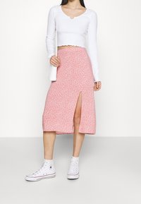 Rosa blommig midikjol med en sidoklyfta, kombinerad med en vit långärmad topp och vita högskaftade sneakers. Slät textur, avslappnad design.