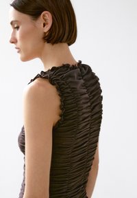 Brown sleeveless dress with ruched fabric, featuring a ruffled neckline and structured silhouette, emphasizing texture and form.