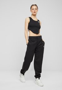 Must have mustekohveriga lühike tank top, millel on sooniline tekstuur, koos laia varsaga mustade dressipükstega, millel on sooniku kumm ja küljetaskud.