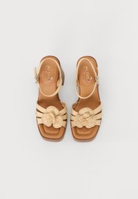 Beige plattform sandaler med vevet blomsterdetalj, skinnsåle og ankelrem. Firkantet tå og strukturert design med teksturert detalj.