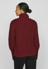 Pull en maille bordeaux avec col montant, texture côtelée et épaules bouffantes. Couleur unie, design simple et coupe décontractée.