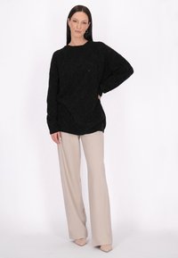 Schwarzer strukturierter Oversized-Pullover mit einem Rautenmuster, kombiniert mit hellbeigen weiten Hosen und nudefarbenen Absätzen.