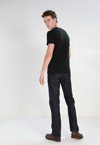 Czarny t-shirt z krótkim rękawem, slim fit, w zestawie z ciemnoniebieskimi dżinsami. Model odwrócony tyłem, odsłania prosty wzór i neutralną kolorystykę.