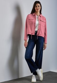 Veste courte rose avec deux poches poitrine, ourlet à cordon, associée à un jean large bleu foncé et des baskets blanches avec des semelles texturées.