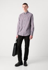 Camicia a maniche corte a scacchi nei colori rosso, blu e bianco, abbinata a pantaloni scuri e scarpe di pelle nere. La persona tiene una borsa tote nera.
