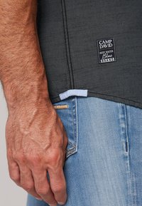 Grijze T-shirt met korte mouwen van textuurstof, voorzien van een zwart merkteken. Gecombineerd met lichtblauwe spijkerbroek met stiksel details.