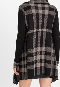 Cardigan a scacchi nero e beige con maniche lunghe, dotato di colletto a scialle e orlo svasato. Texture a maglia, design con schiena aperta.