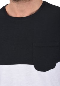 Camiseta de manga corta en blanco y negro con una mezcla de algodón texturizado, con cuello redondo y un bolsillo en el lado izquierdo del pecho.