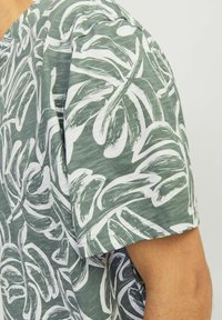 Korte mouwen T-shirt in groene stof met een wit bladerenpatroon; heeft een ronde hals en een textuur op het oppervlak gemaakt van zacht, ademend materiaal.