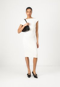 White fitted dress with short sleeves, smooth texture, mid-calf length. Paired with a small black handbag and black pointed heels.