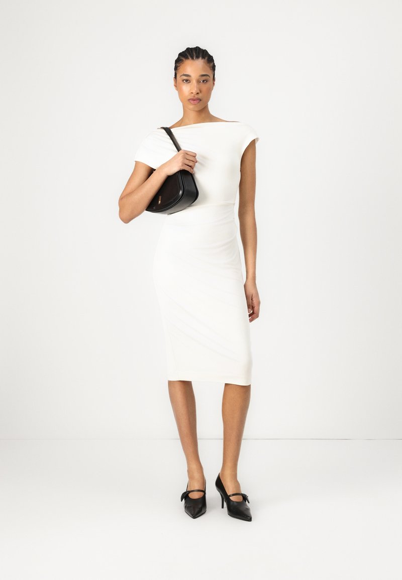 White fitted dress with short sleeves, smooth texture, mid-calf length. Paired with a small black handbag and black pointed heels.