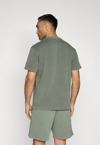 Short-sleeve, olive green t-shirt made of cotton, features a relaxed fit with visible stitching and a soft, smooth texture.