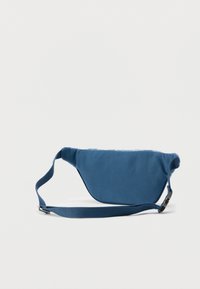 Μπλε υφασμάτινη τσάντα μέσης με λείο υφή, καμπυλωτό σχήμα, ρυθμιζόμενο λουράκι και μινιμαλιστικό σχεδιασμό. Διαθέτει ασφαλές κούμπωμα με τοκά.