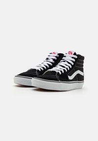 Baskets montantes noir et blanc avec lacets blancs, semelles épaisses blanches et bande blanche latérale sur chaque chaussure, présentées en angle.