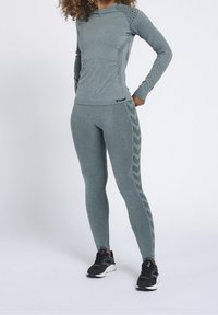 Woman wearing matching grey athletic leggings and long-sleeve top with chevron patterns, standing with hands on hips.