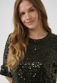 Melnas paildētām piespraudēm topiņš ar īsām piedurknēm, apaļu kakla izgriezumu un nedaudz brīvu piegriezumu. Iespējas spīdīga, atstarojoša virsma un mīksta tekstūra.