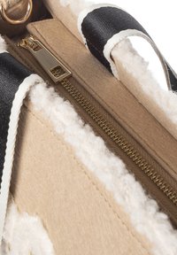 Beige tas met een zachte, gestructureerde buitenkant en zwarte stoffen hengsels. Geaccentueerd met een gouden ritssluiting en witte, zachte voering.