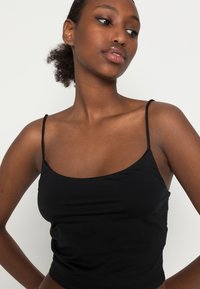 Camisola preta ajustada com alças finas, feita de um material liso e elástico, apresentando um decote redondo e um design simples.