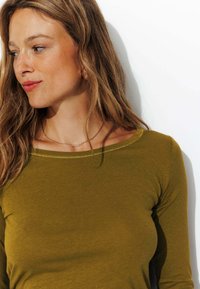 Haut à manches longues vert olive avec un col rond, présentant de délicites coutures le long du bord. Texture douce et lisse. Design simple.