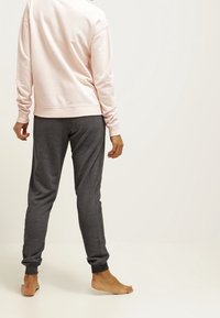 Sudadera rosa clara con cuello redondo y puños acanalados, combinada con joggers gris oscuro con puños elásticos en los tobillos.