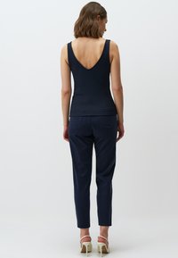 Top in cotone navy a costine con scollatura profonda a V sul retro, abbinato a pantaloni navy slim-fit. L'outfit è completato da sandali con tacco di colore chiaro.