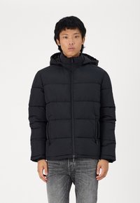 Svart boblejakke med glidelås foran, hette og sidelommer. Laget av glatt, lett stoff med en quiltet design og synlig søm.