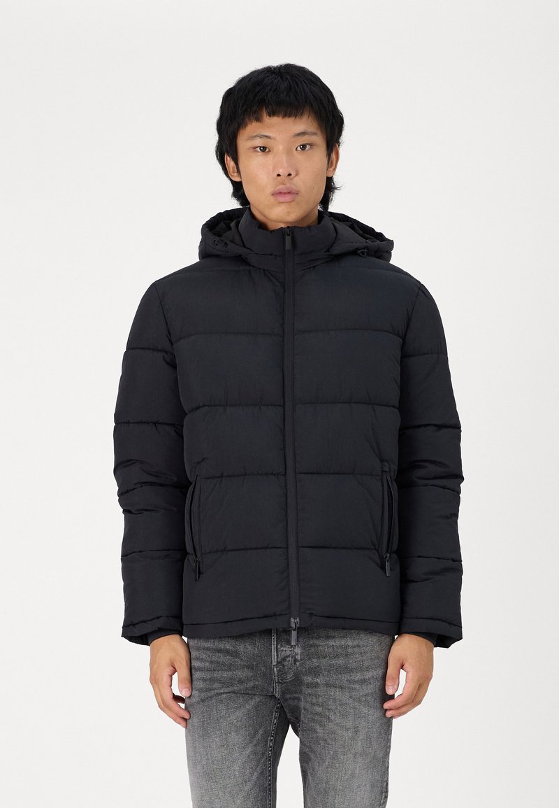 Svart boblejakke med glidelås foran, hette og sidelommer. Laget av glatt, lett stoff med en quiltet design og synlig søm.