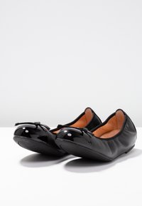 Mustat ballerinat, joissa on sileä nahkapinta ja kiiltävä lakattu kärki. Edessä pieni rusetti ja pehmeä sisävuori.