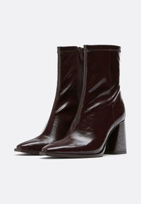 Stivaletti bordeaux realizzati in materiale lucido e liscio, con punta affusolata e tacco spesso e chunky. Presentano una cerniera laterale per una facile calzata.