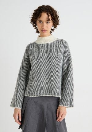 Grijze en witte herringbone gebreide trui met een hoge nek en wijde klokmouwen, met een zachte textuur en een cropped lengte.
