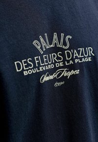 Υφασμα σε ναυτικό μπλε χρώμα με λευκό κείμενο που αναγράφει Palais des Fleurs d'Azur, Boulevard de la Plage, Saint-Tropez και τον αριθμό 3990.