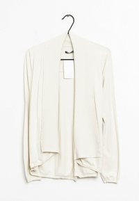 Ljus beige cardigan tillverkad av mjukt stickat material, med öppen front, långa ärmar och en sjalkrage med ribbade detaljer.