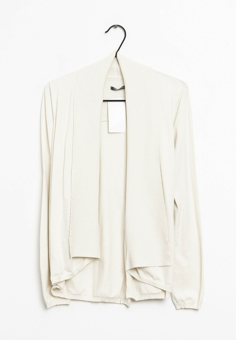 Ljus beige cardigan tillverkad av mjukt stickat material, med öppen front, långa ärmar och en sjalkrage med ribbade detaljer.