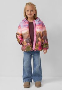 Geplüschte Jacke mit einem bunten Farbverlauf-Design, das Pferde und Blumen zeigt. Mit Kapuze, pinkem Reißverschluss und elastischen Bündchen. Kombiniert mit ausgestellt geschnittenen Jeans.