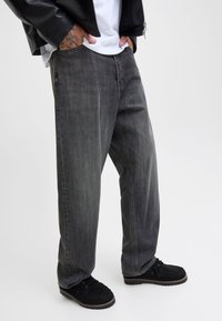 Pelēkas džinsa bikses ar vaļīgu piegriezumu, piecām kabatām un smalku izbalējumu. Kombinētas ar melniem zamšādas apaviem.