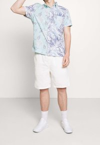 Koszula z krótkim rękawem w miętowym kolorze z niebieskimi kwiatowymi wzorami, zestawiona z białymi szortami i białymi trampkami dla swobodnego stylu.